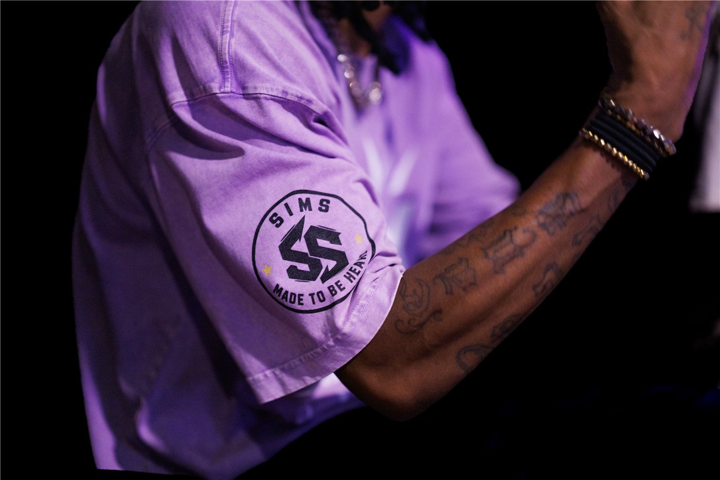 Close-up of the Sims Made To Be Heard logo on a purple tee worn at a BMC event